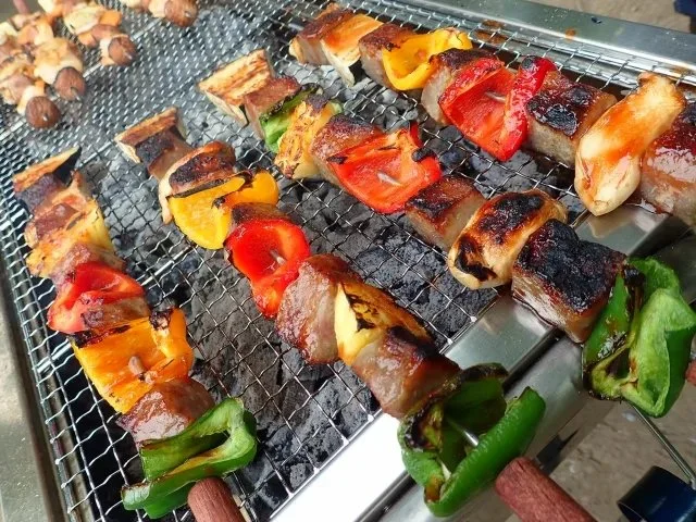 バーベキューグリルで肉と野菜の串焼きを炭火で焼いている様子