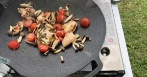 JHQマルチグリドルで鶏肉・キノコ・ミニトマトを焼いているキャンプシーン