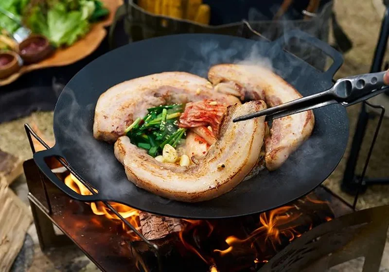 JHQマルチグリドルで豚肉をキャンプファイヤーで焼いている様子
