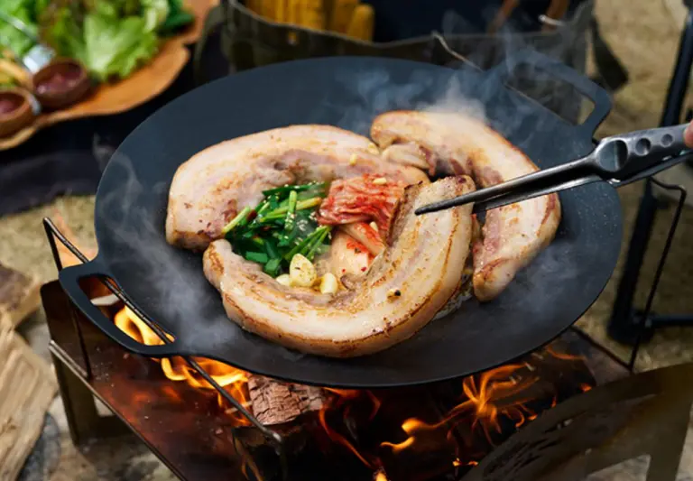 マルチグリドルで直火を使い豚肉とキムチを焼いているキャンプシーン