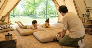 テント内で電動ポンプを使ってインフレーターマットをふくらませる父親と子どもたち