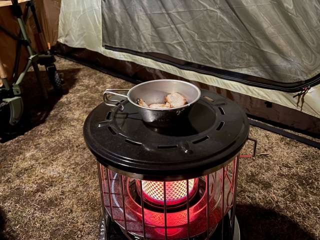 キャンプ用ストーブの天板でシェラカップの料理を温めている様子
