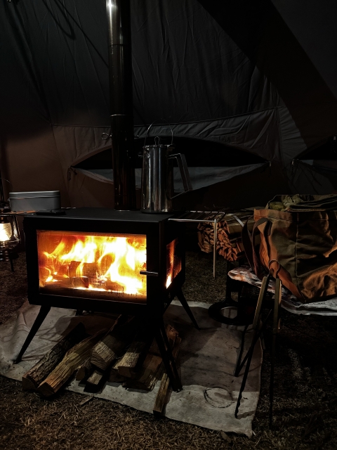 夜のキャンプサイトで焚き火のように暖かく燃える薪ストーブ