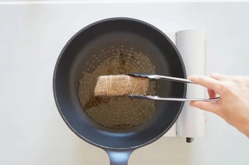 テフロンフライパンでトングを使って肉を焼いている様子