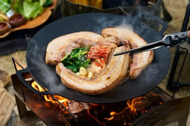 焚き火の上のマルチグリドルでお肉と野菜を焼いている様子